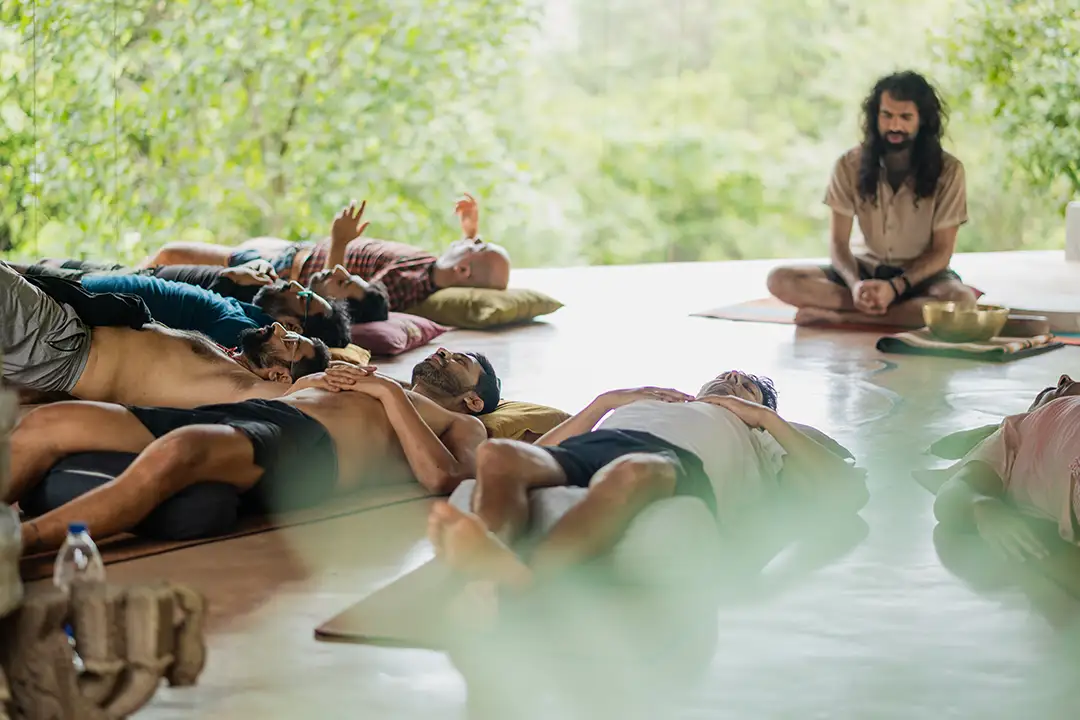 Men lying on mats in a breathwork session with a facilitator sitting nearby.