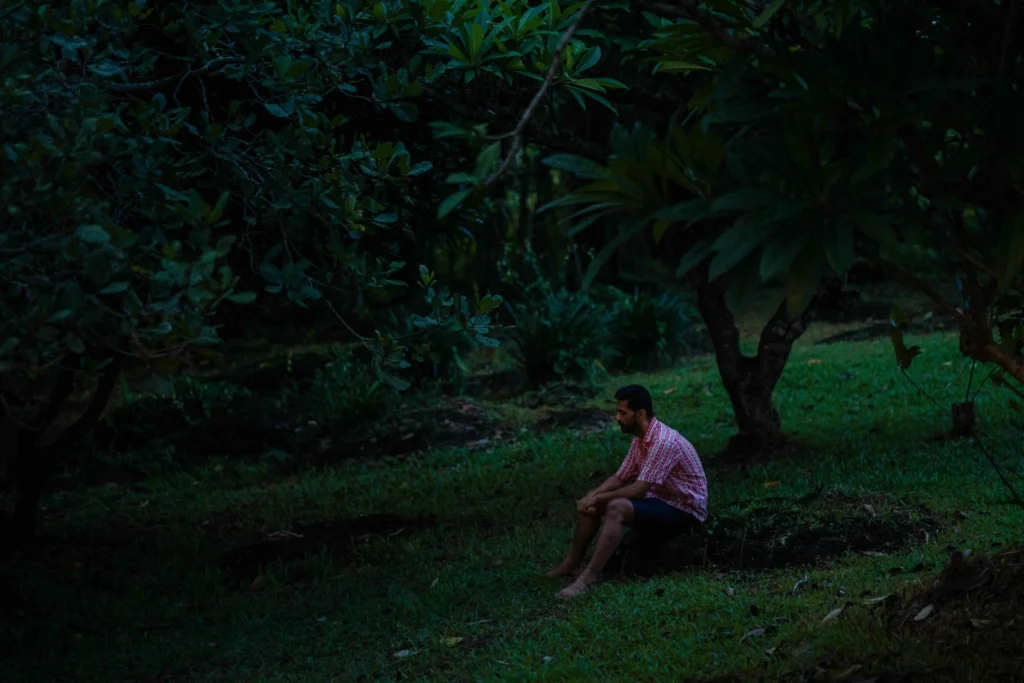 Man sitting barefoot in a forest clearing — a quiet moment of stillness and reflection.