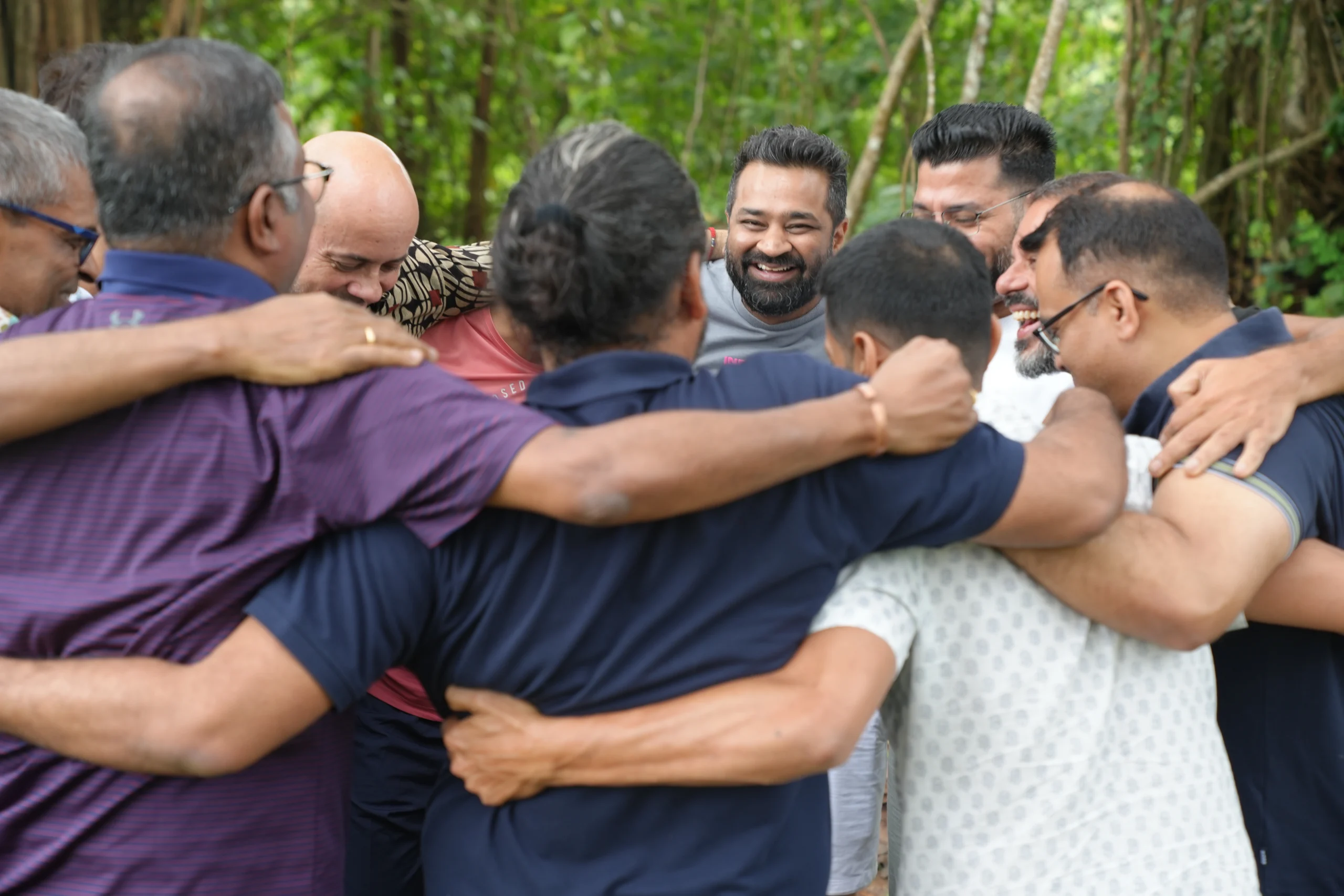 Men standing in a circle with arms around each other, sharing a joyful moment of connection.